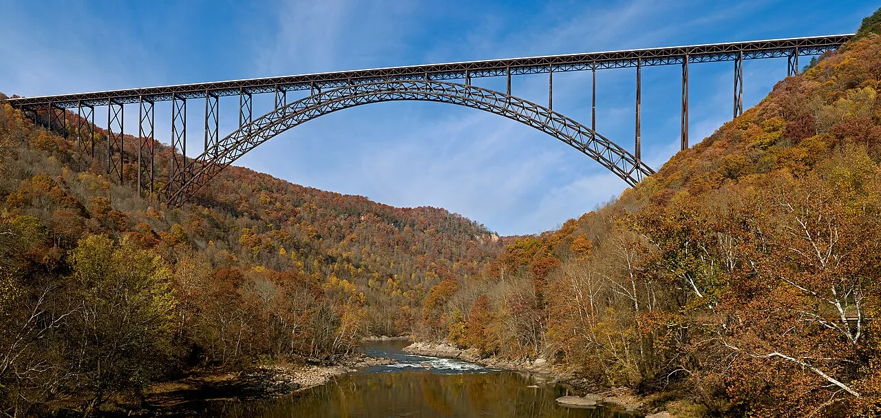 An arched bridge spanning a river between wooded hills