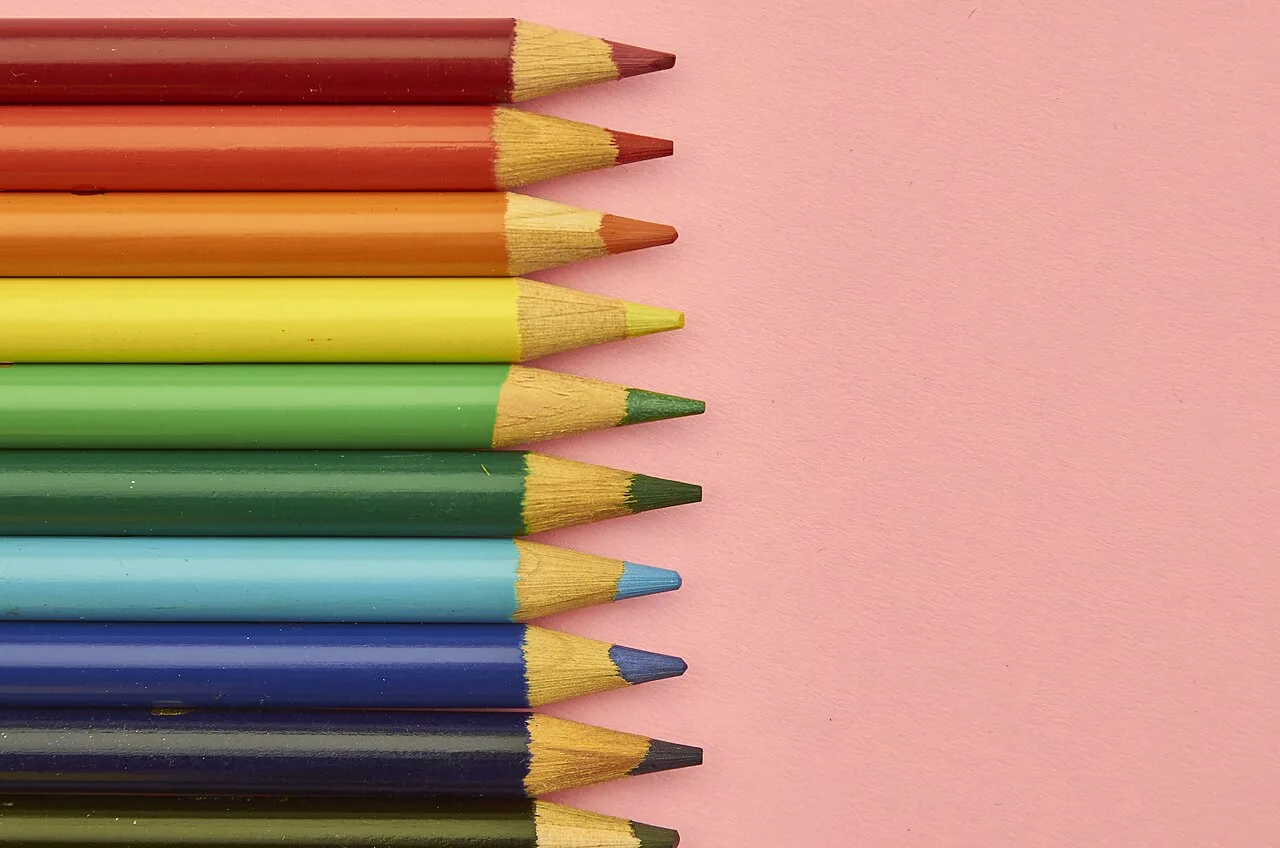 Colored pencils lined up on a pink surface