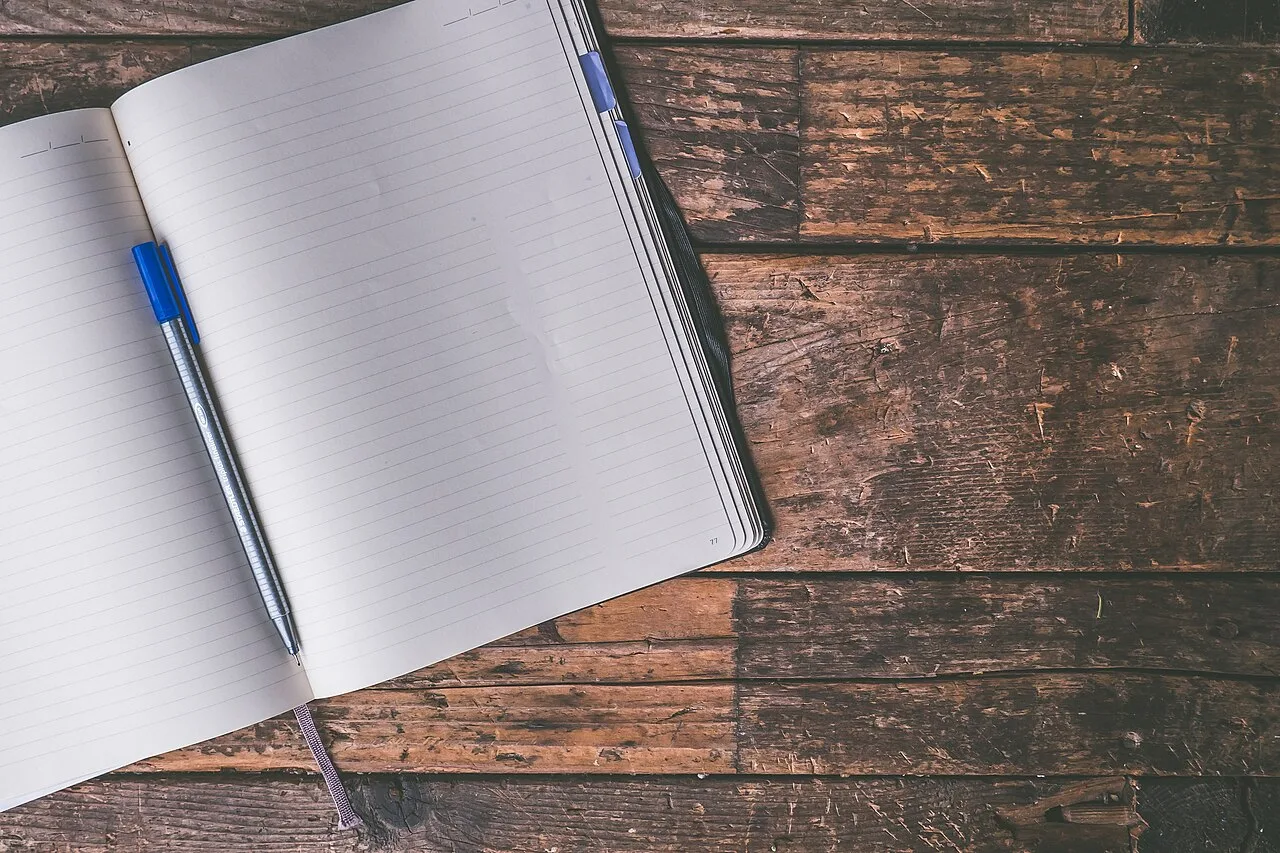 An open blank notebook and pen on a wooden surface