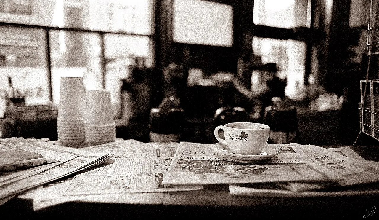 A coffee cup and newspaper on a cafe table