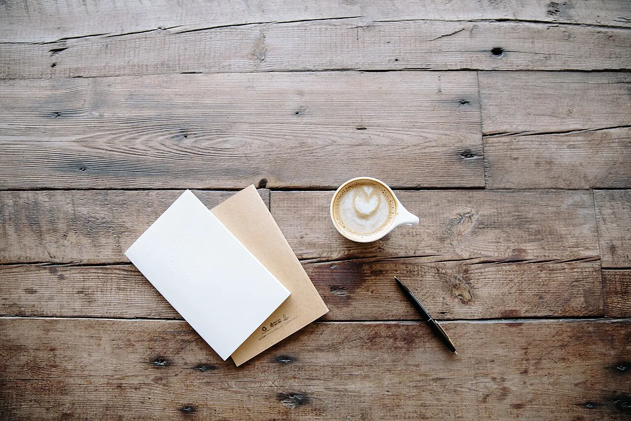 An open notebook and coffee cup on a weathered wooden table