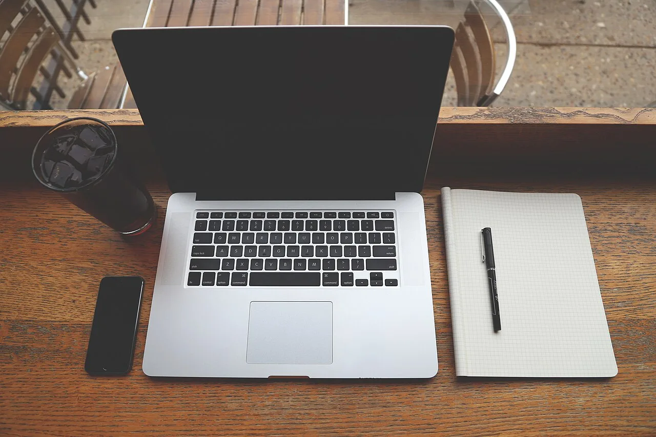 A laptop and blank notebook arranged on a wooden desk