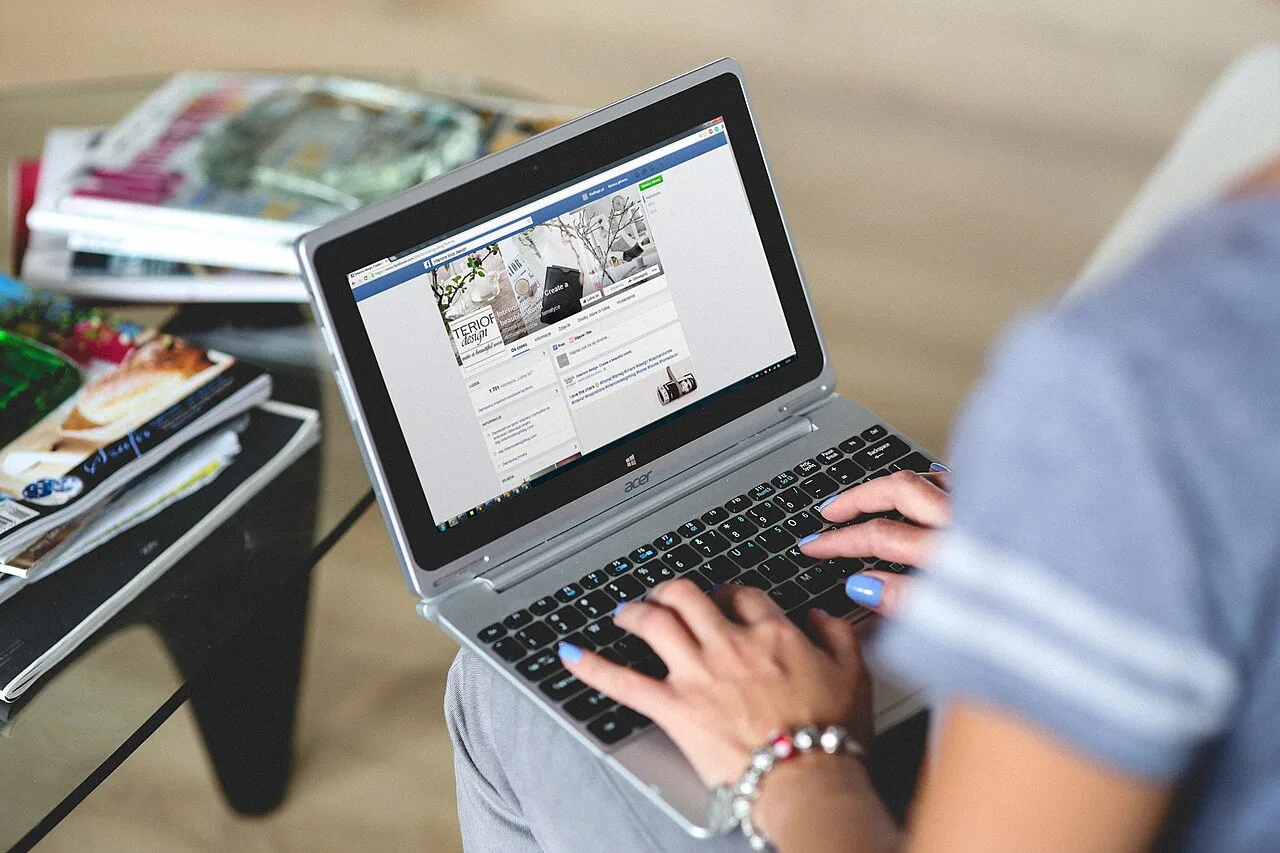 Hands using a laptop while seated beside books and reading material