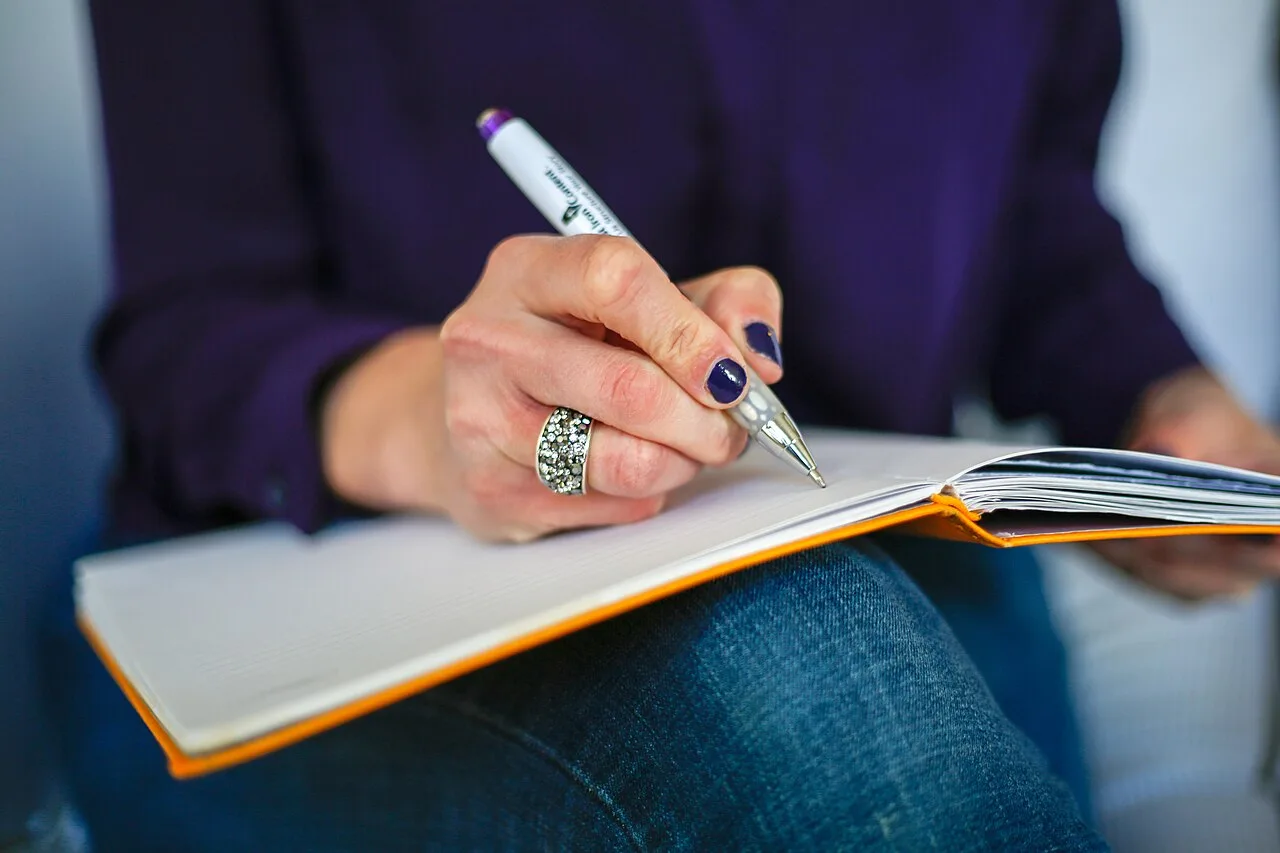 Hands writing in a notebook resting on a lap