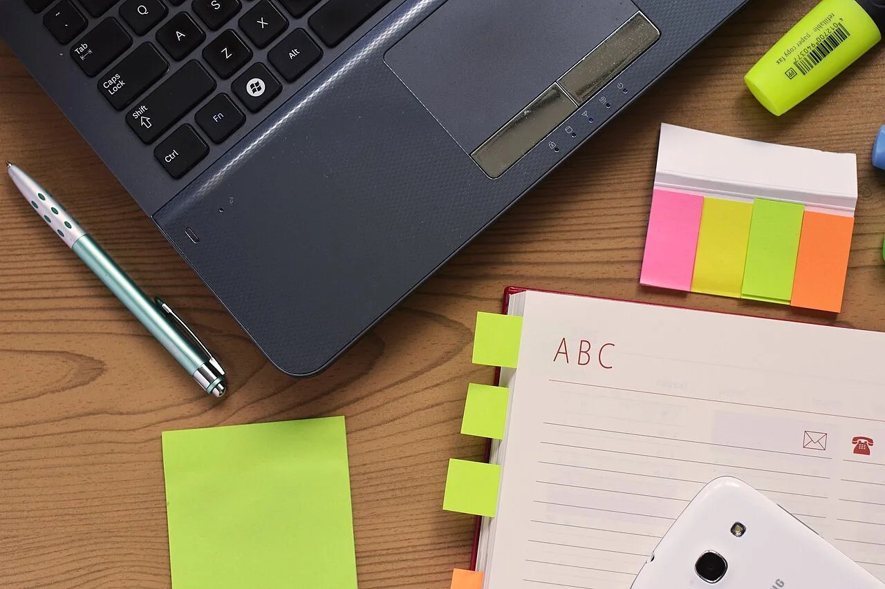 A laptop, notes, and colored page markers on a desk