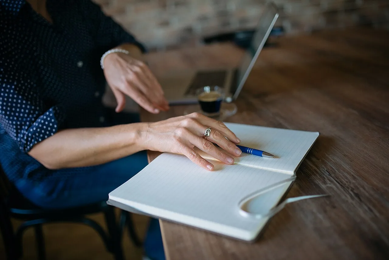Hands writing in a notebook at a cafe table