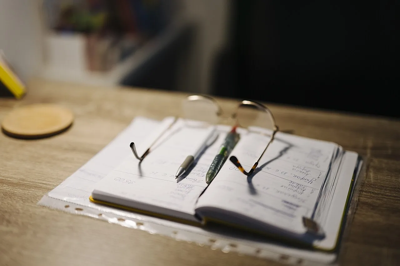 A notebook, pens, and glasses laid out on a desk