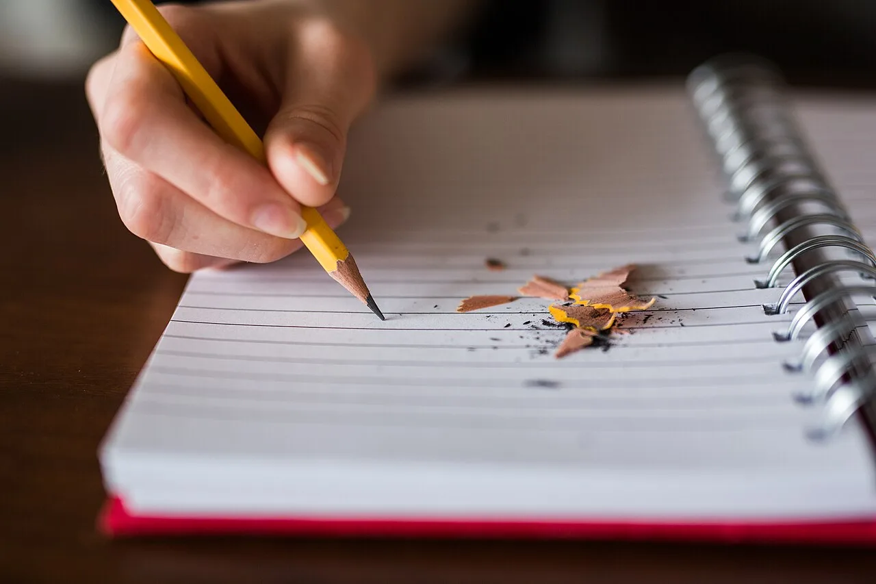 A hand making notes with a pencil in a lined notebook