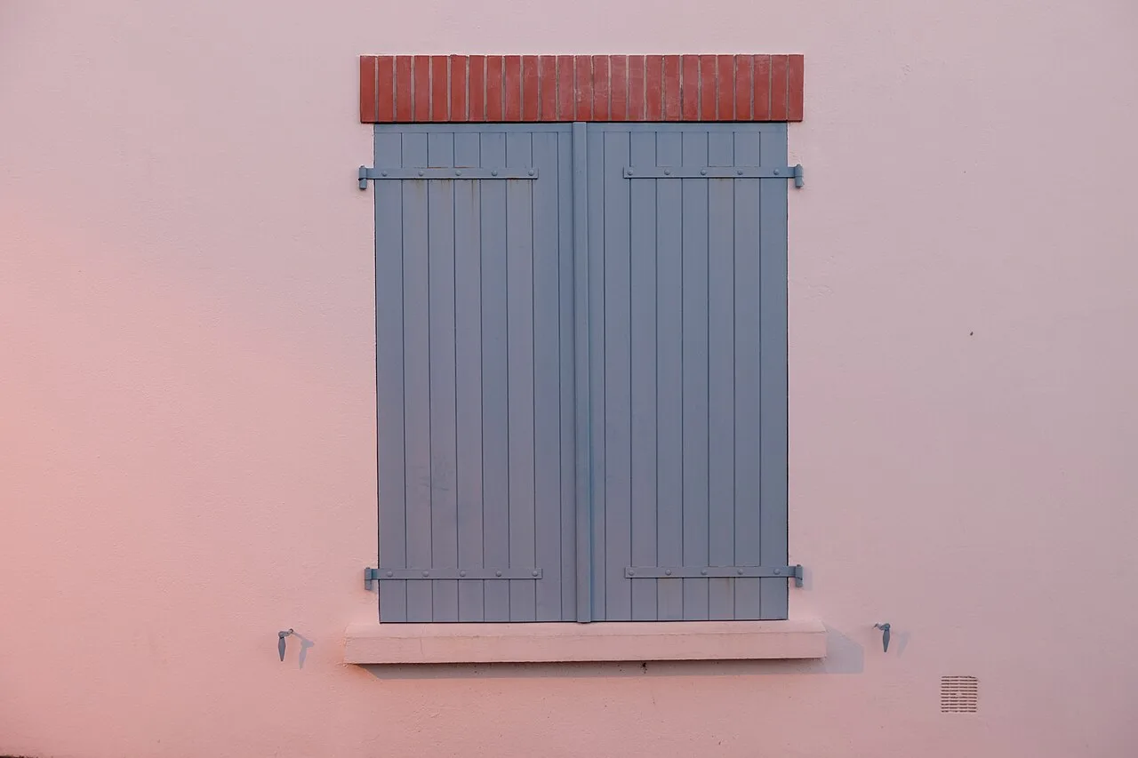 Closed blue shutters on a pale pink wall