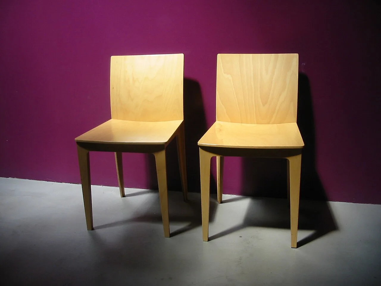 Two wooden chairs side by side against a plum-colored wall