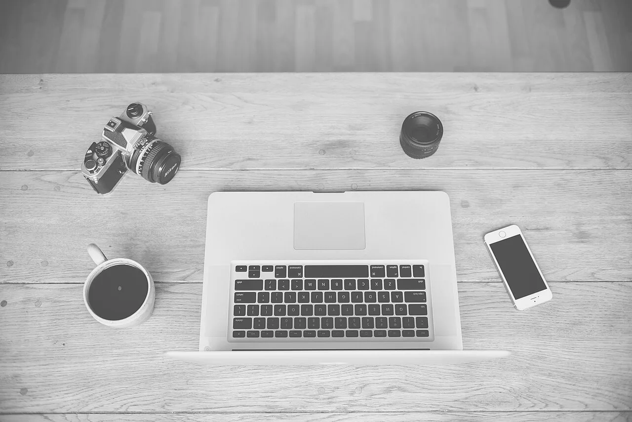 A laptop, phone, coffee cup, and camera on a wooden desk